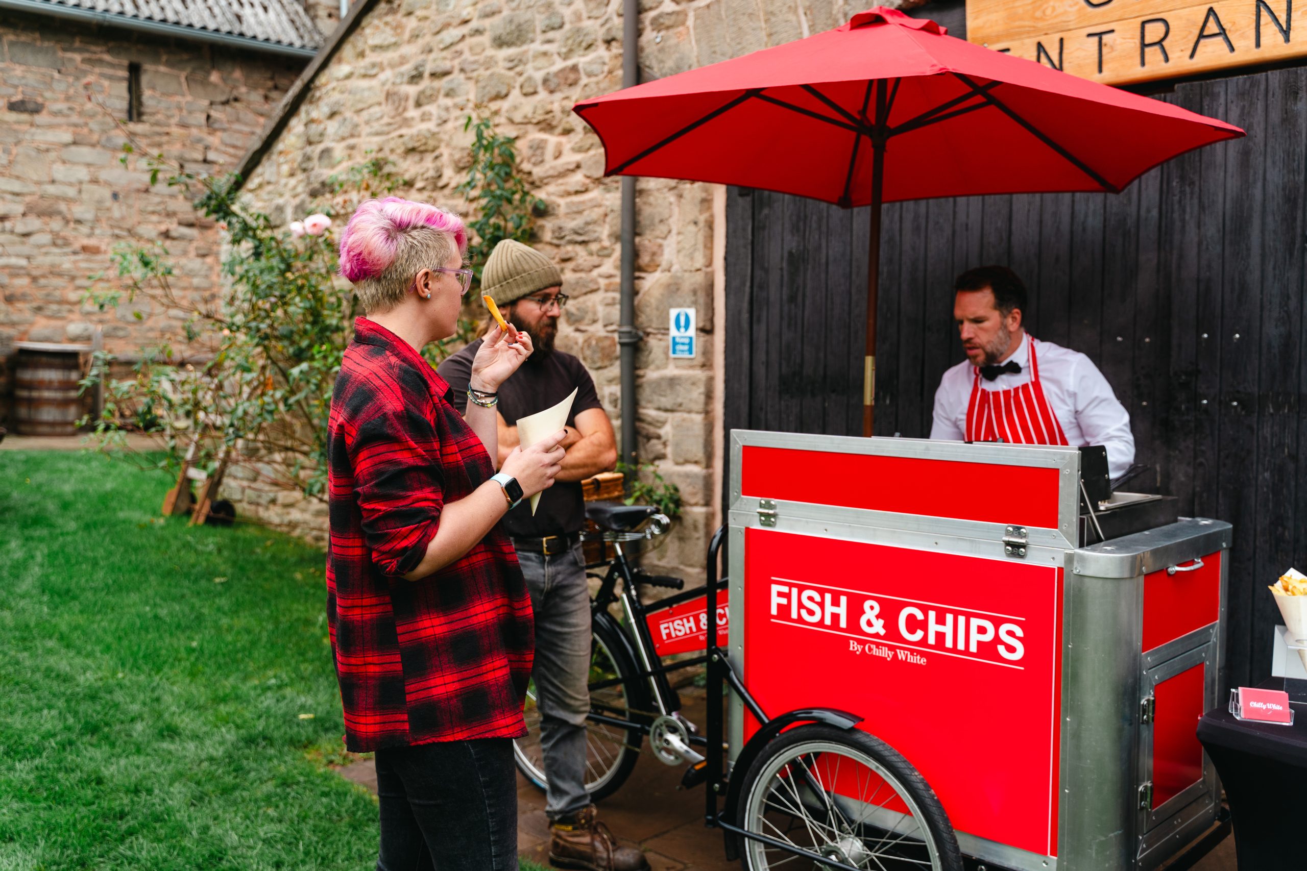 Fresh fish and chips stand at outdoor event with vendor under red umbrella in UK.