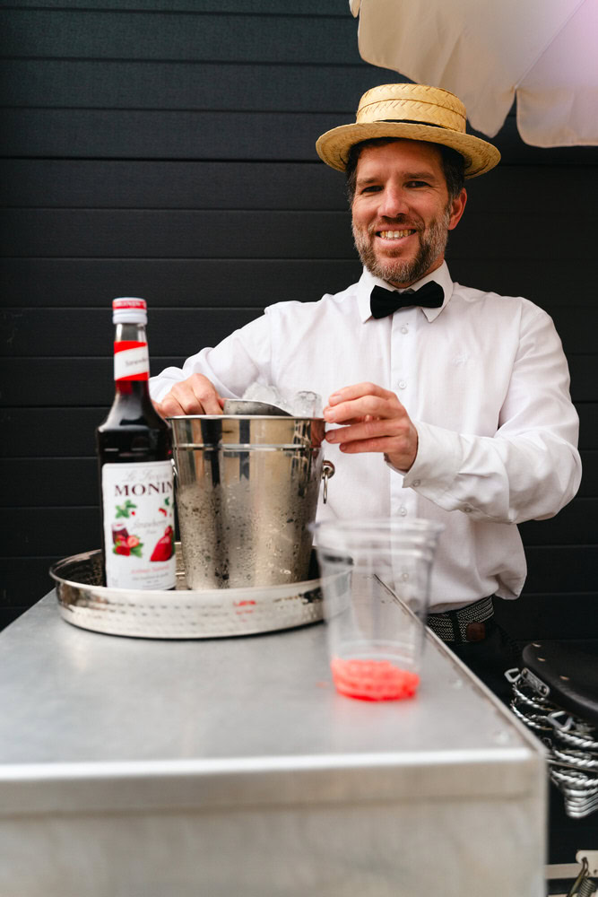Refreshing cocktail preparation by a bartender in vintage attire at outdoor event.