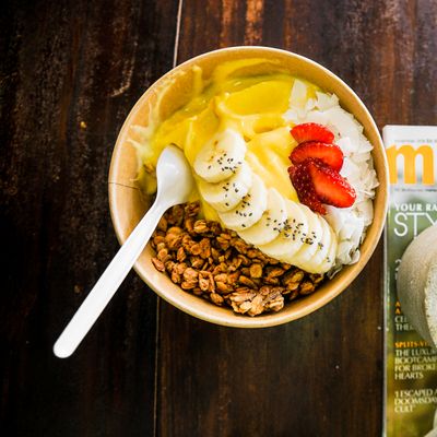 Close-up of a yogurt bowl with granola, banana, and strawberries on a wooden table.